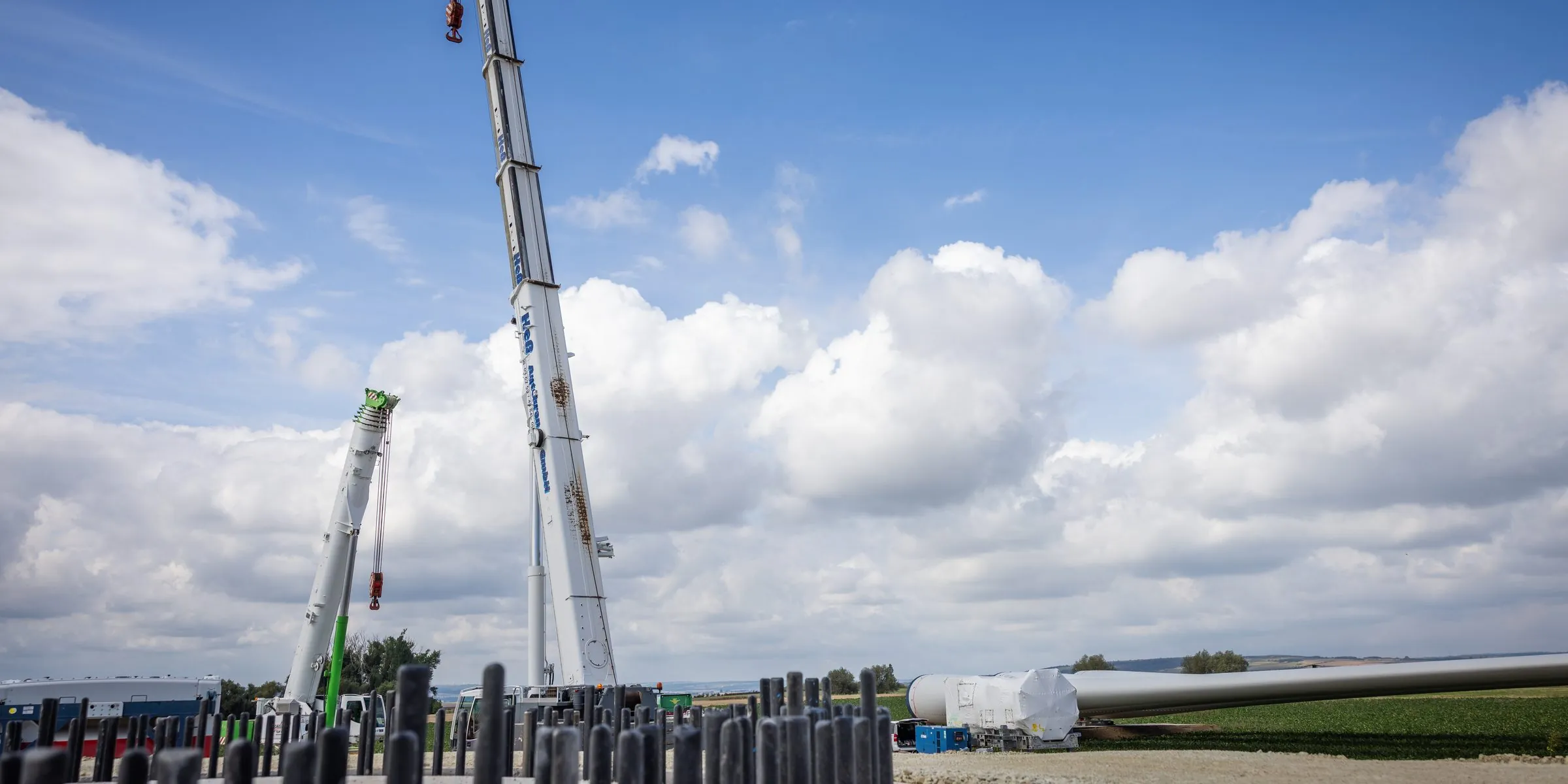Zwei ausgefahrene Autokrane vor blauem Himmel mit Wolken auf einer Windpark-Baustelle