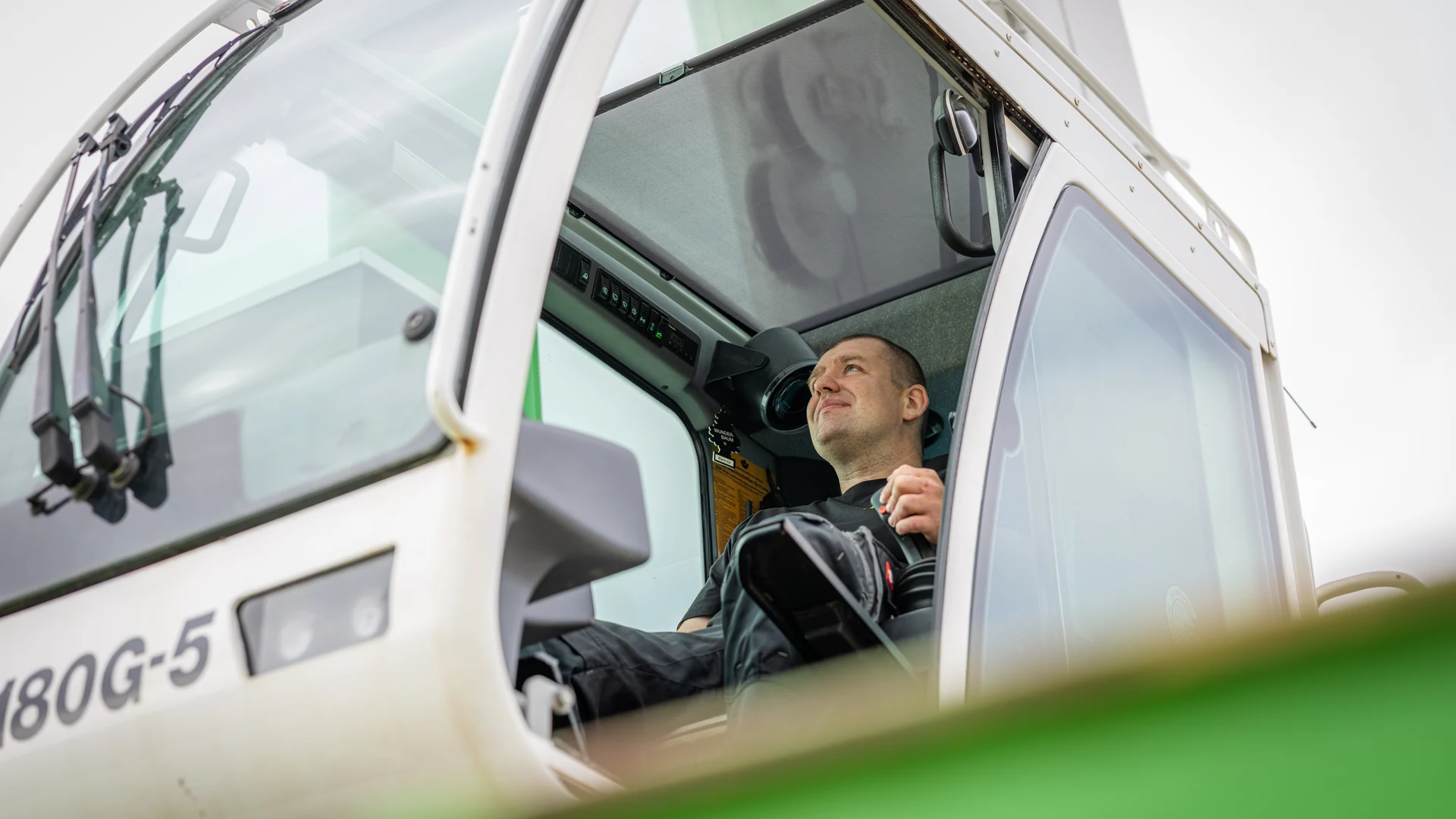 Lächelnder Kranfahrer in der Kabine eines weißen Autokrans