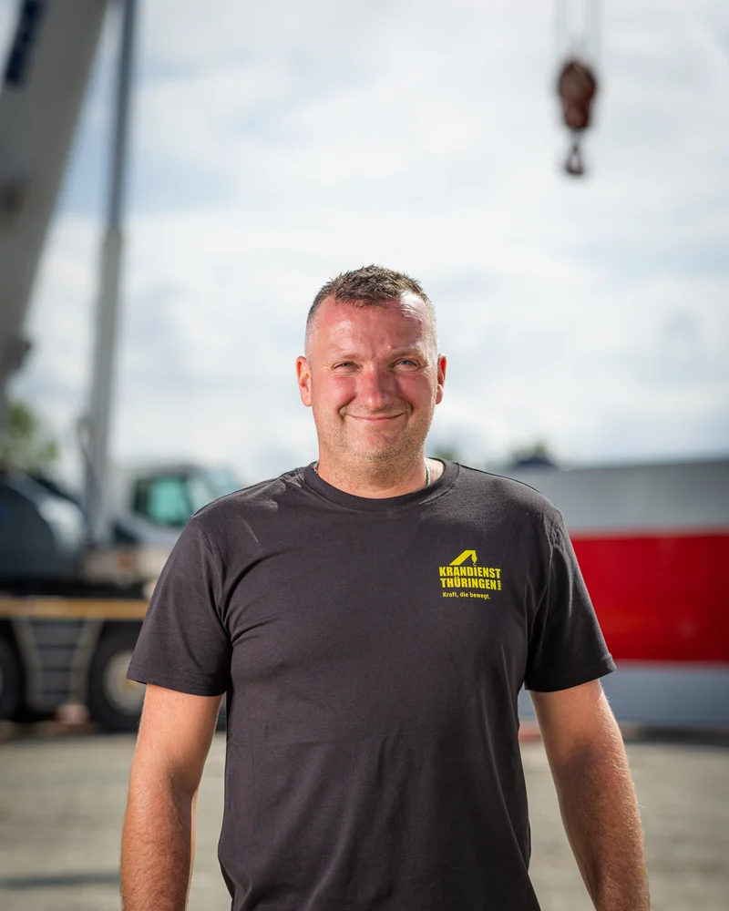 Mitarbeiter von Krandienst Thüringen in Arbeitshose auf der Baustelle, im Hintergrund ein Lasthaken