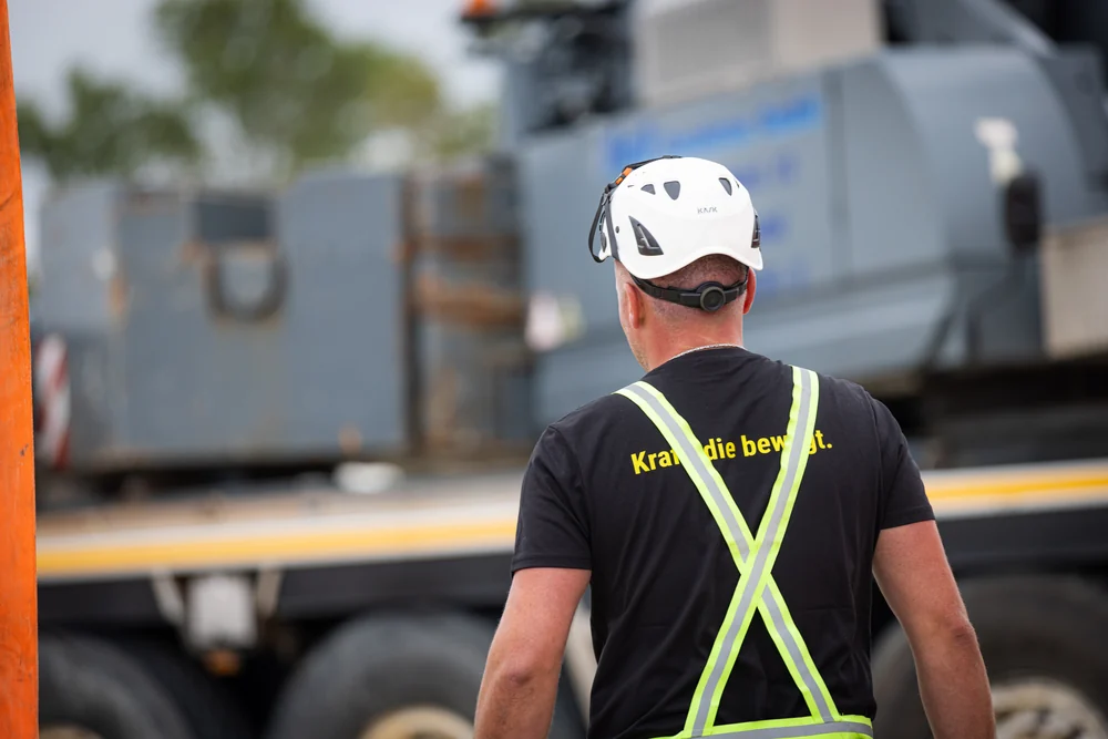 Mitarbeiter mit Schutzhelm und Warnweste von hinten, auf dem Shirt steht Kraft, die bewegt.