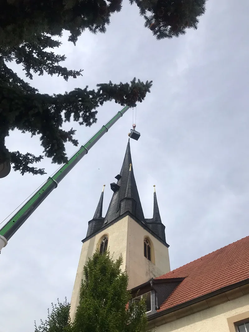 Ausleger eines Autokrans ragt neben einem Kirchturm in den Himmel