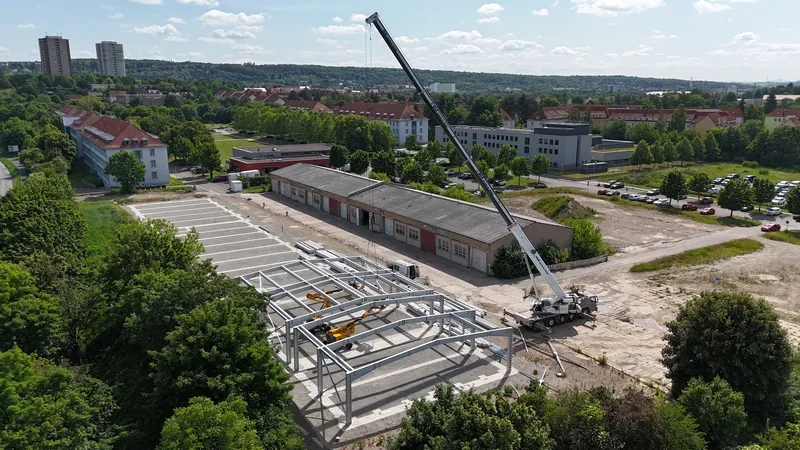 Autokran montiert das Stahltragwerk einer Halle, Blick von oben auf die Baustelle